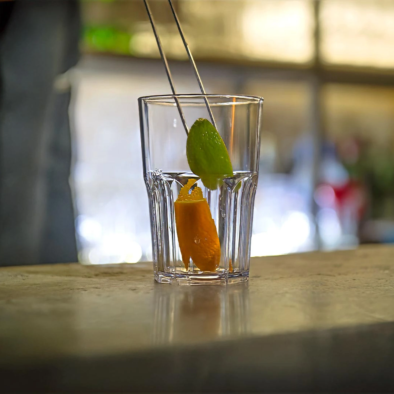 Kunststof glazen Granity Clear 400 ml op de bar, sinaasappelschil en limoen geplaatst met een garneerpincet